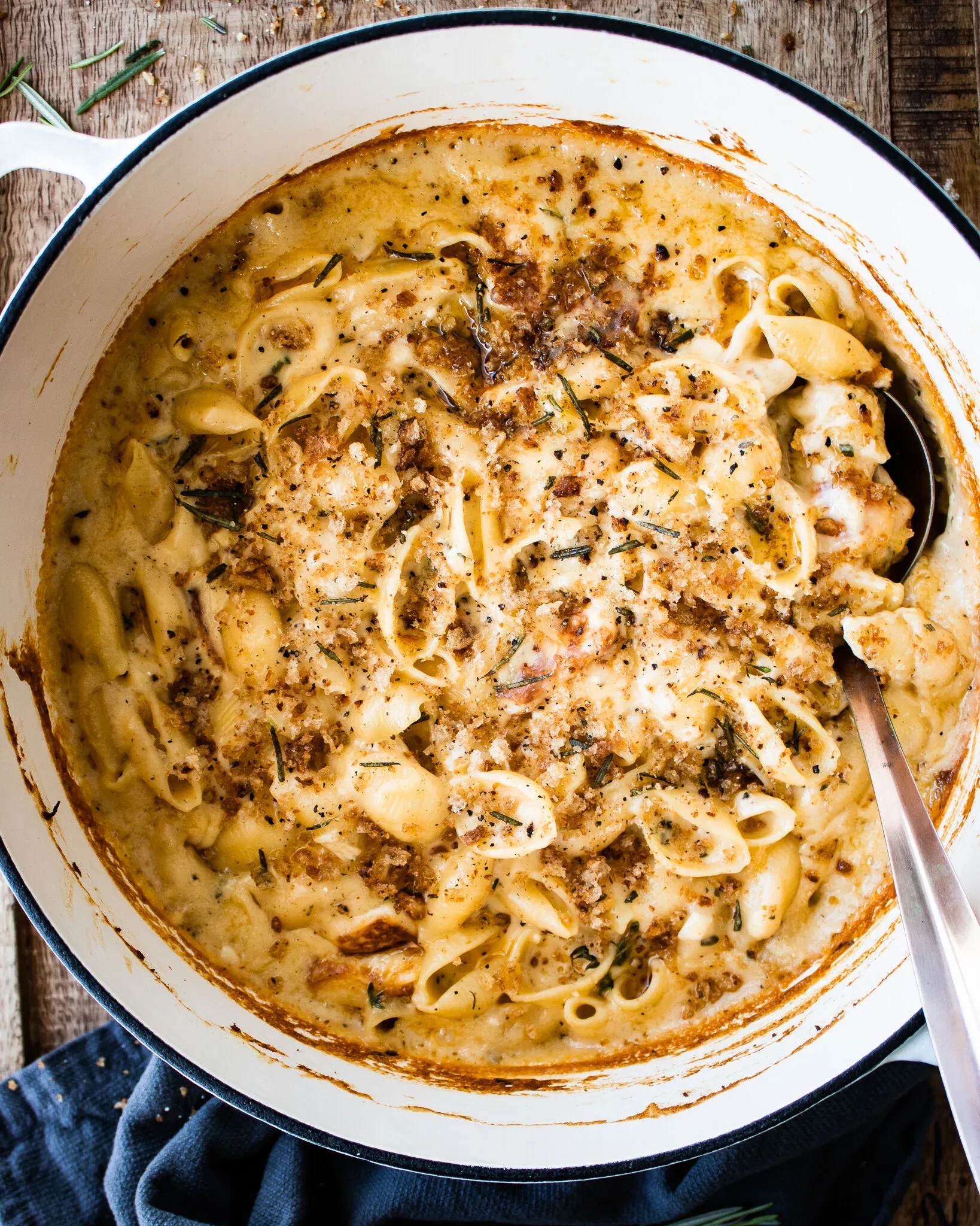 Wide overhead view of the finished 7 Cheese Herb and Garlic Baked Mac and Cheese in a white enamel Dutch oven with a large serving spoon resting in the dish