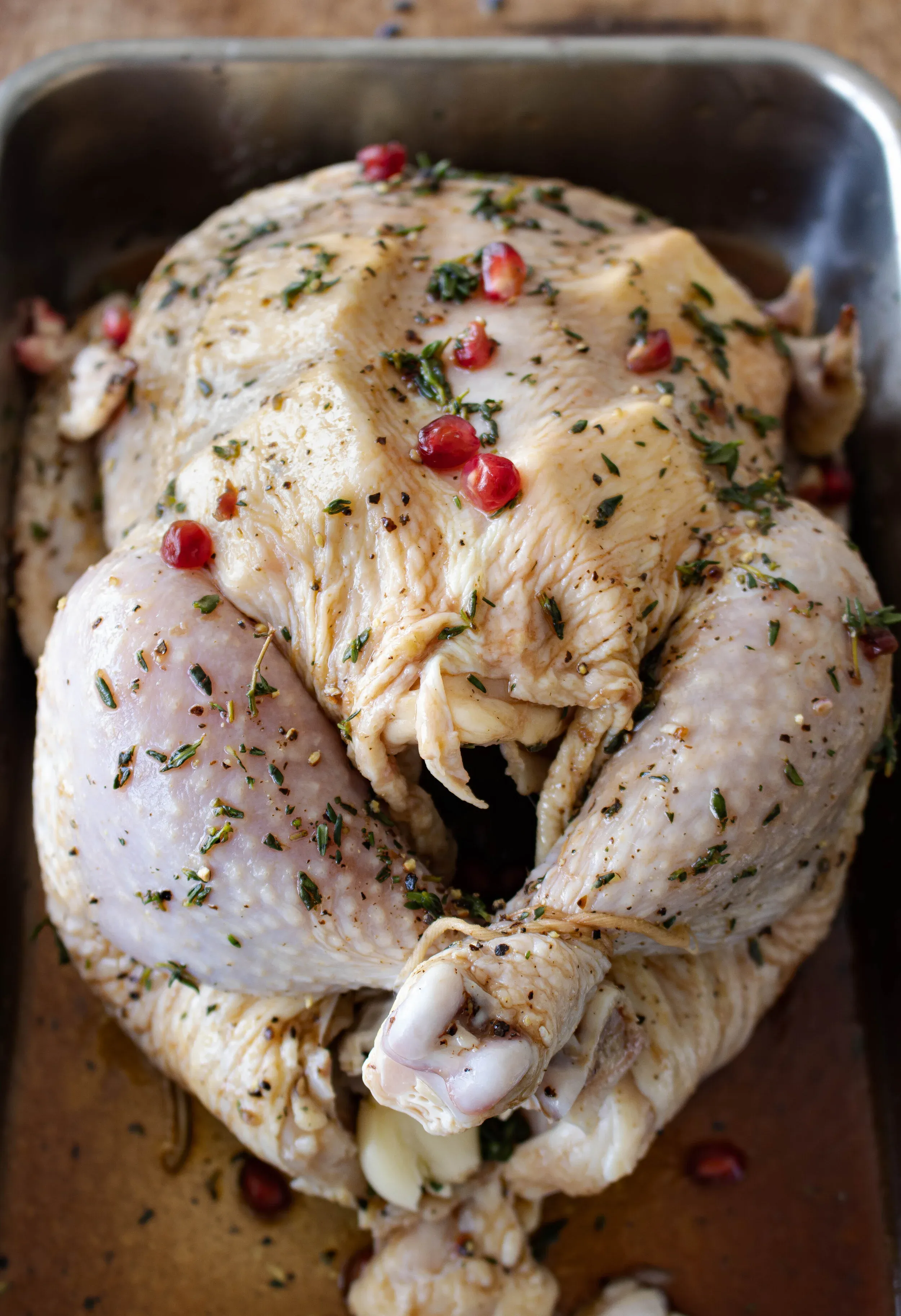 Raw whole chicken marinated in an herb and pomegranate mixture in a silver roasting pan