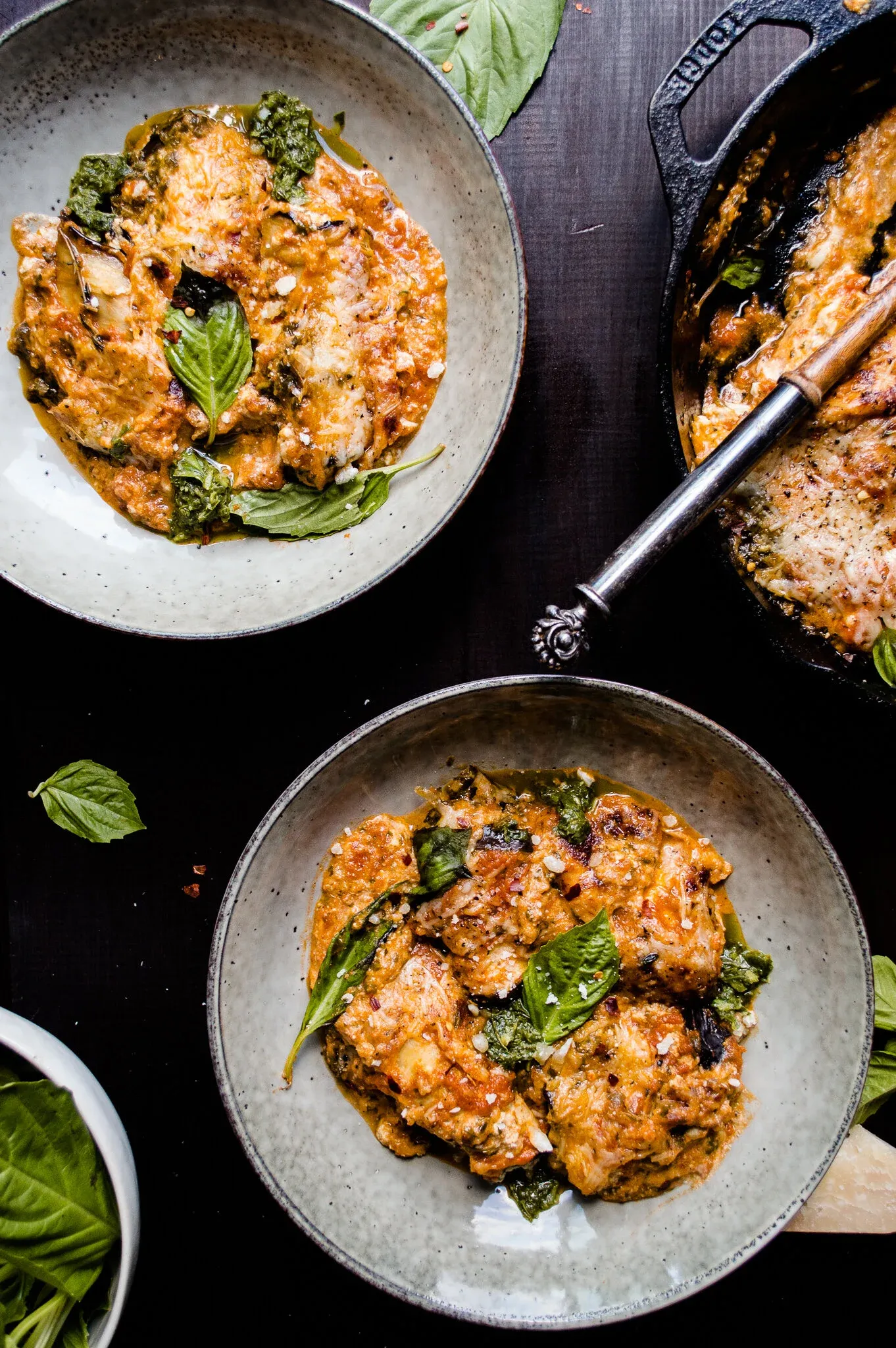 Overhead flat-lay of two grey speckled stoneware bowls each holding a serving of Eggplant Involtini