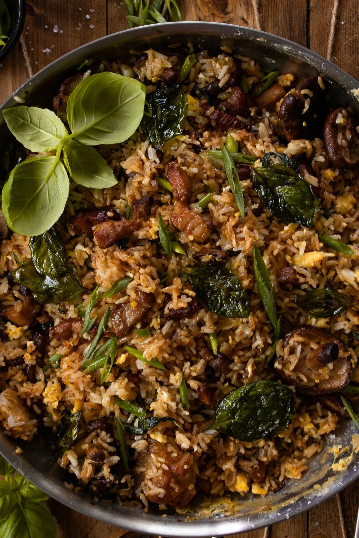 Close-up overhead view of pork belly, mushroom and crispy basil fried rice in the stainless steel pan