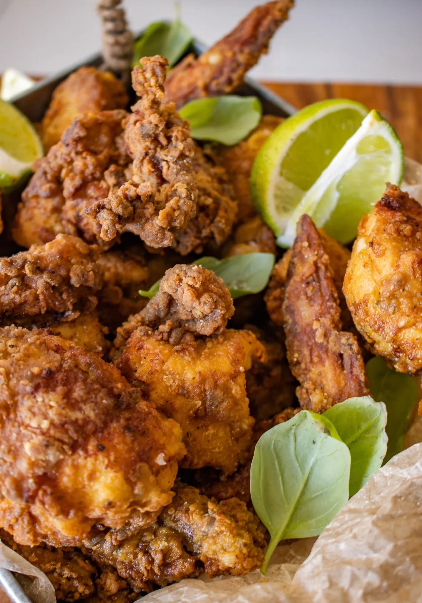 Close-up side view of Dominican pica pollo fried chicken in a parchment-lined metal tray showing the deeply textured
