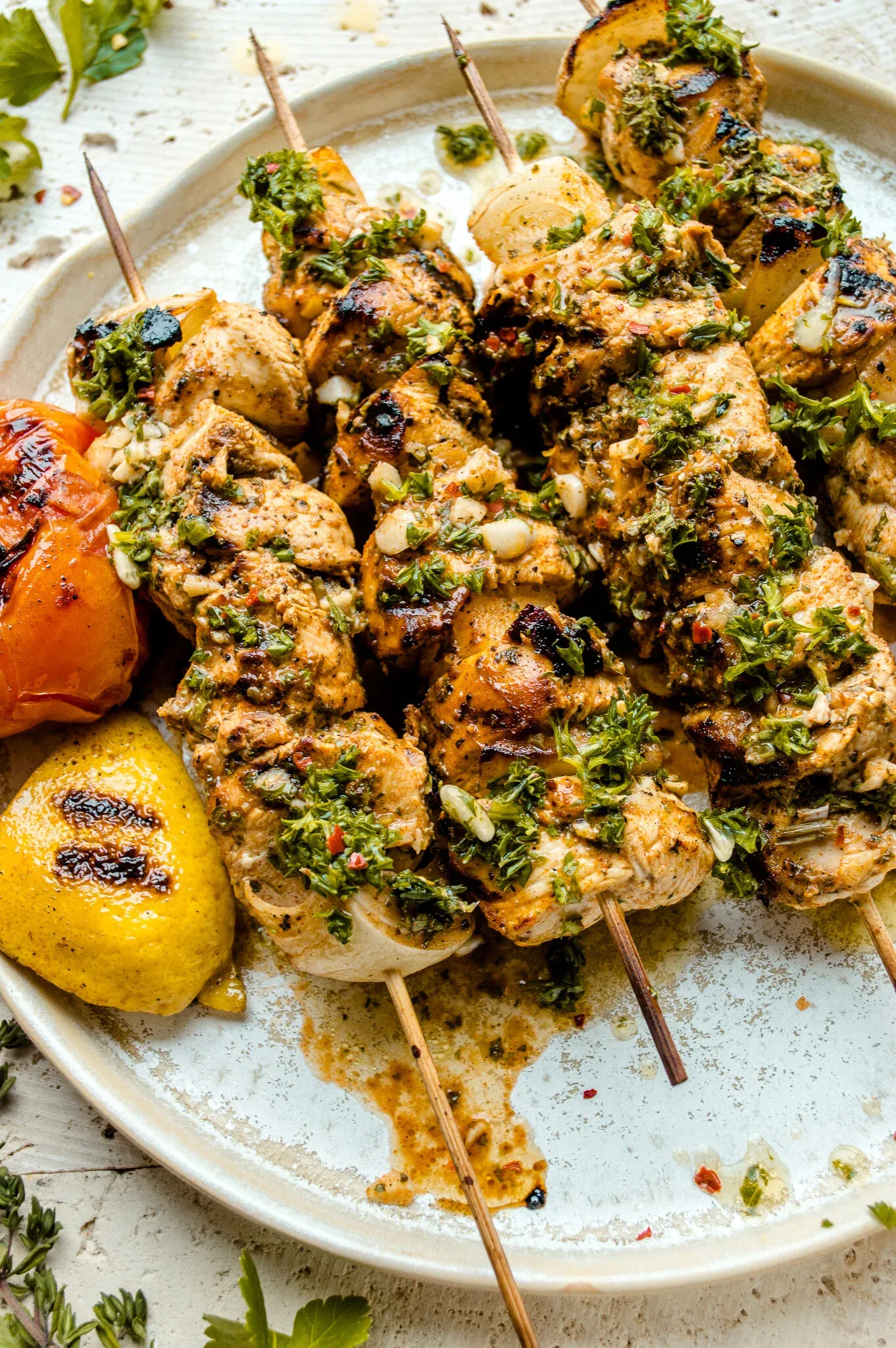 Angled close-up of grilled chicken skewers on a white ceramic plate showing the deep grill marks and golden-brown seared exterior of the chicken pieces