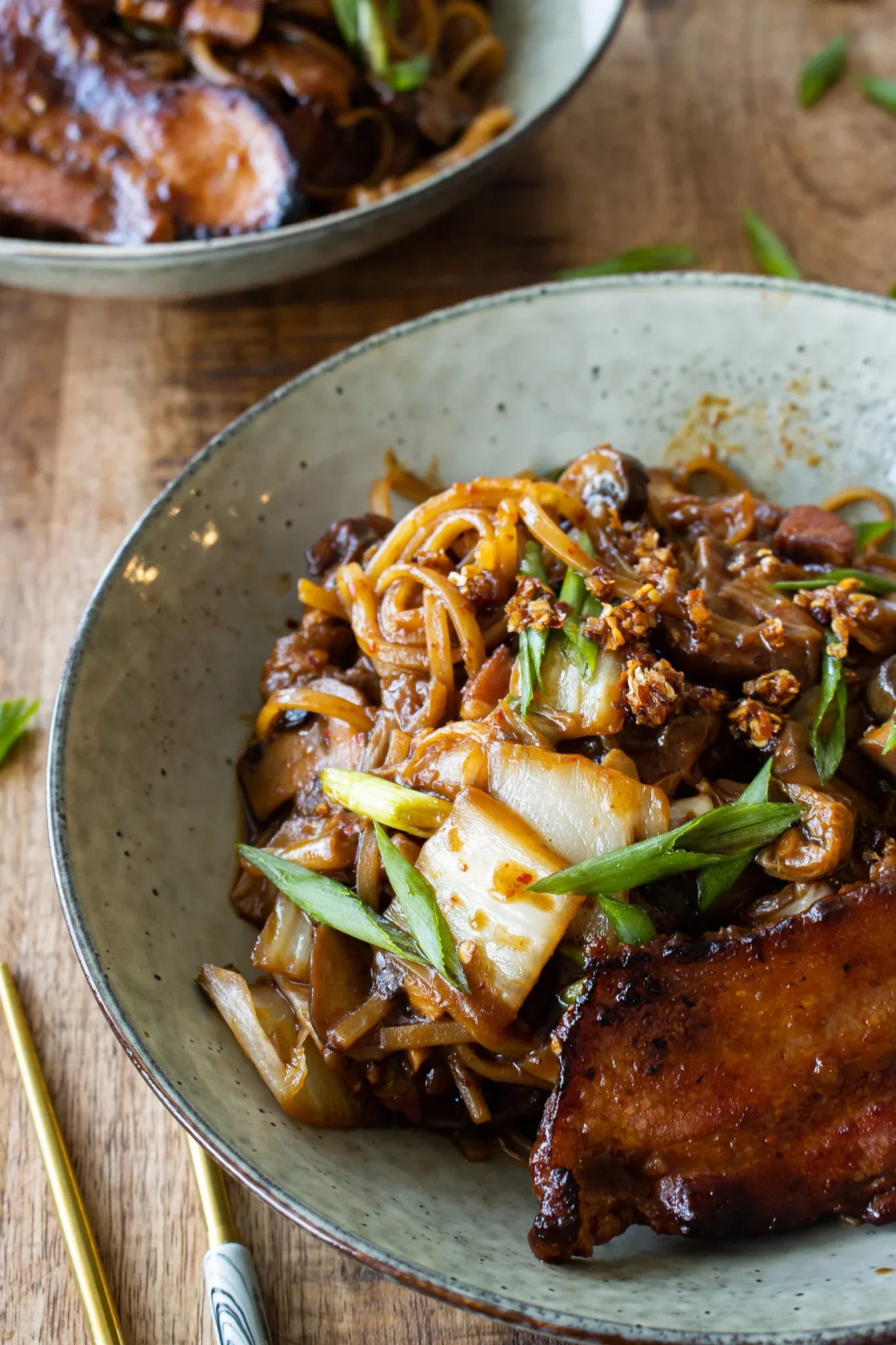 Angled close-up of a speckled gray ceramic bowl of chili crisp noodles with pan-fried pork belly