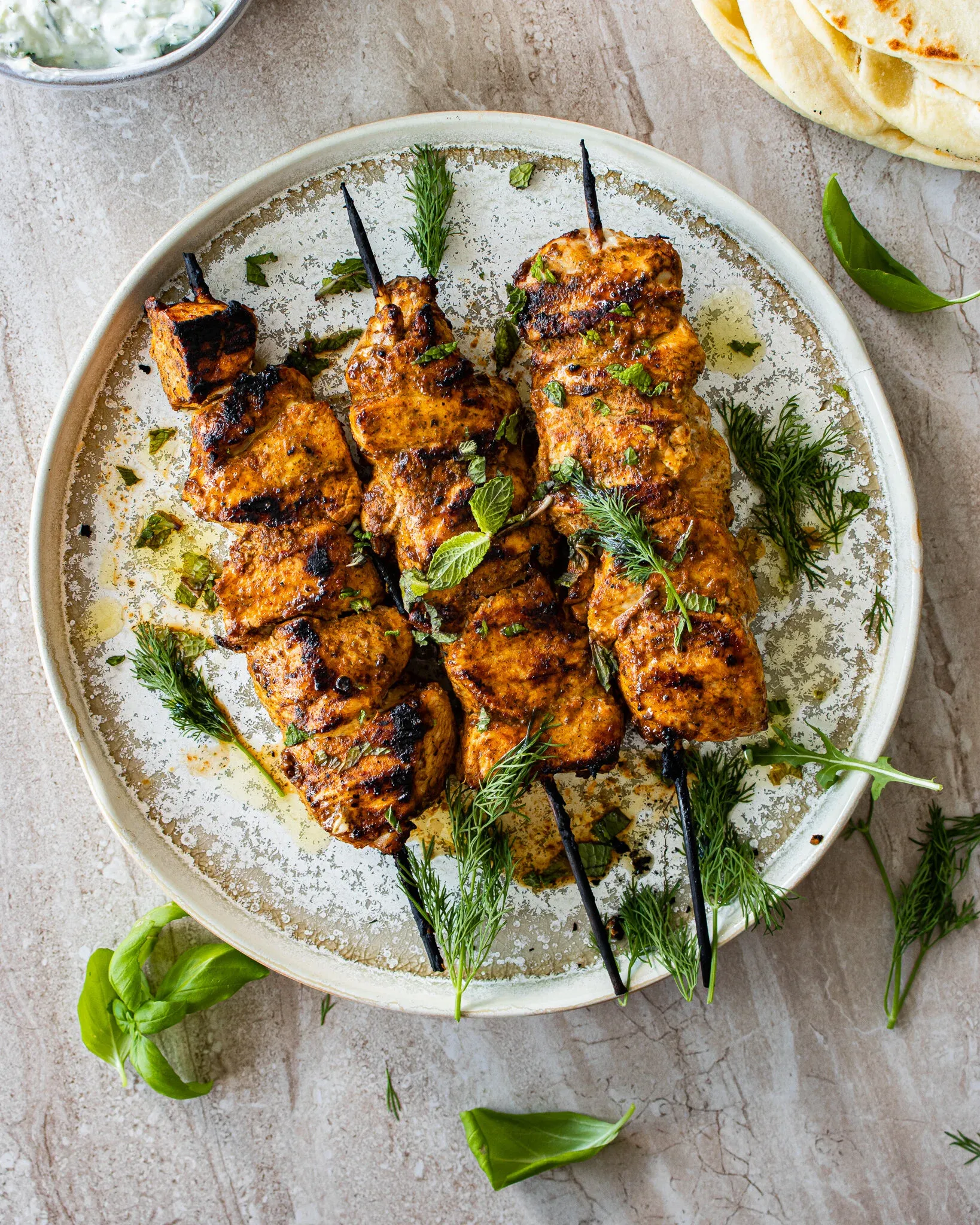 Overhead view of four spiced chicken skewers on a rustic white ceramic plate