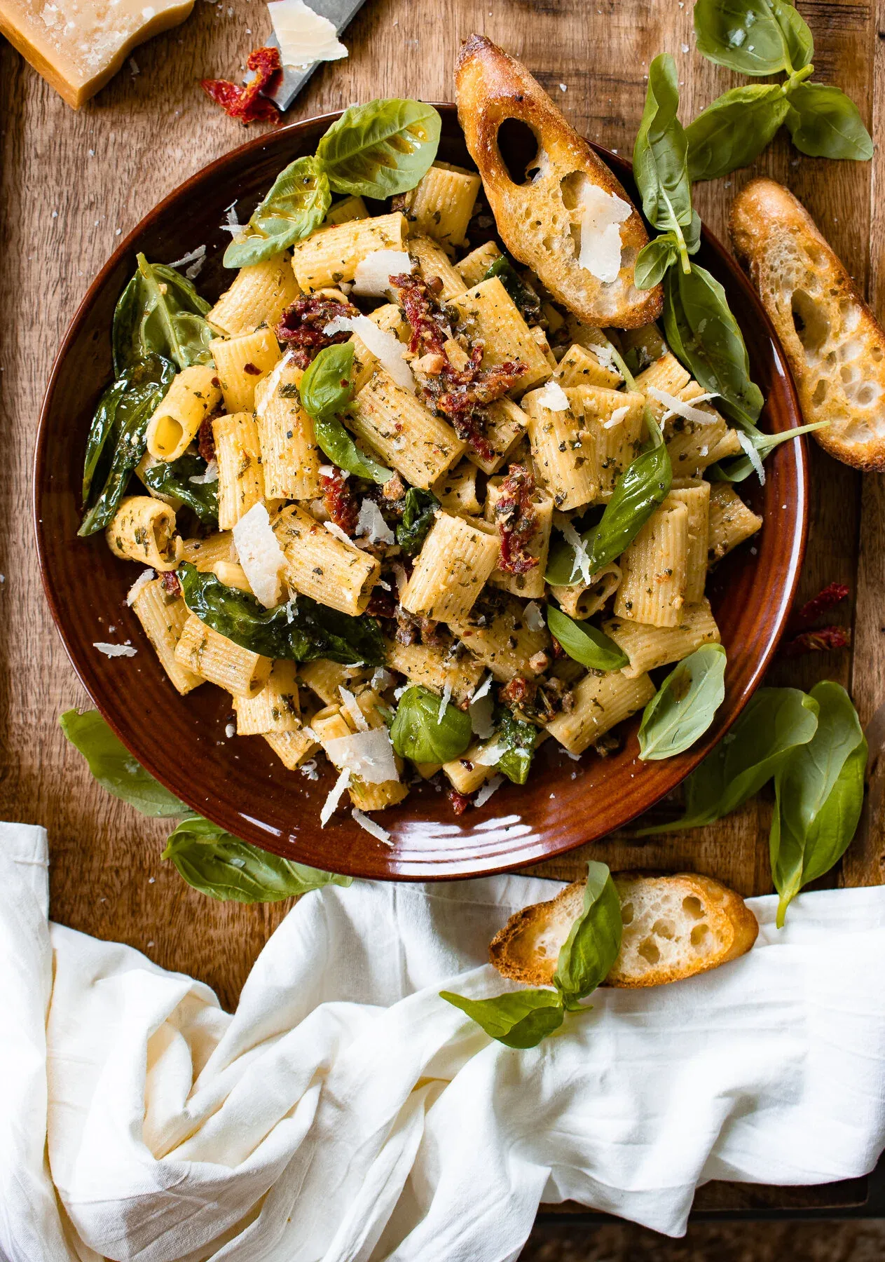 Wide overhead shot of the 30 Minute Basil Pasta with Sun-Dried Tomatoes in the dark terracotta bowl showing the full herb-tossed rigatoni with sun-dried tomatoes and Parmesan shavings