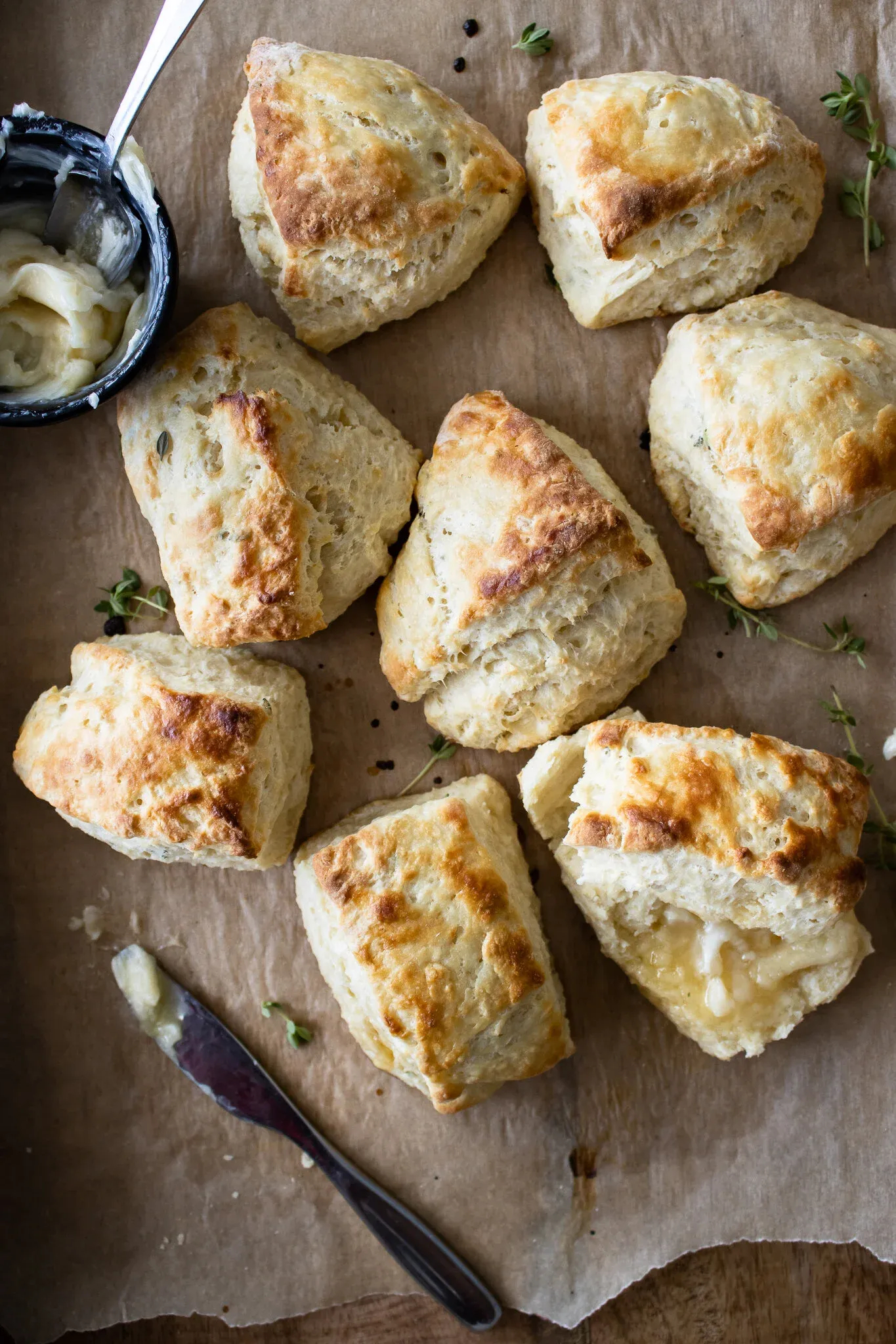 Overhead arrangement of seven triangular golden-brown lemon thyme buttermilk biscuits on brown parchment paper over a wood surface