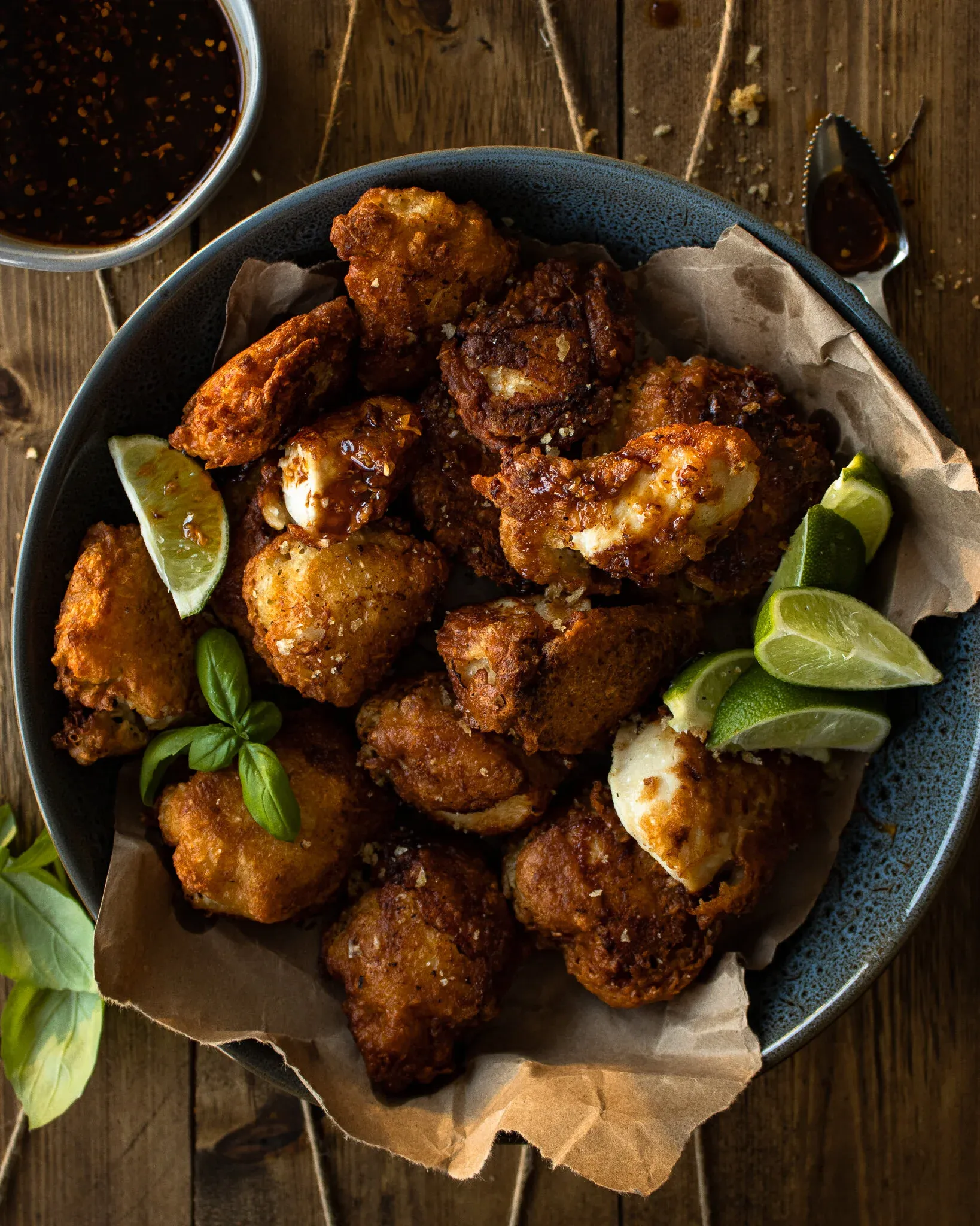 Overhead view of Batter Fried Chicken in the dark blue bowl with a drizzle of dark chili-soy dipping sauce pooling on some of the golden-brown fried pieces