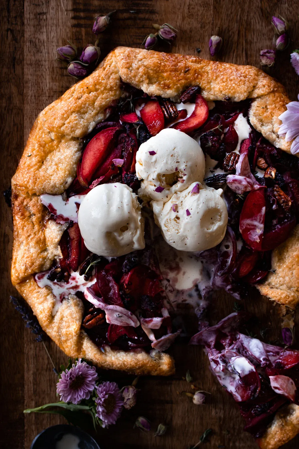 Angled overhead view of the finished poached peach galette with melting vanilla ice cream pooling into the dark burgundy wine-poached peach and pecan filling