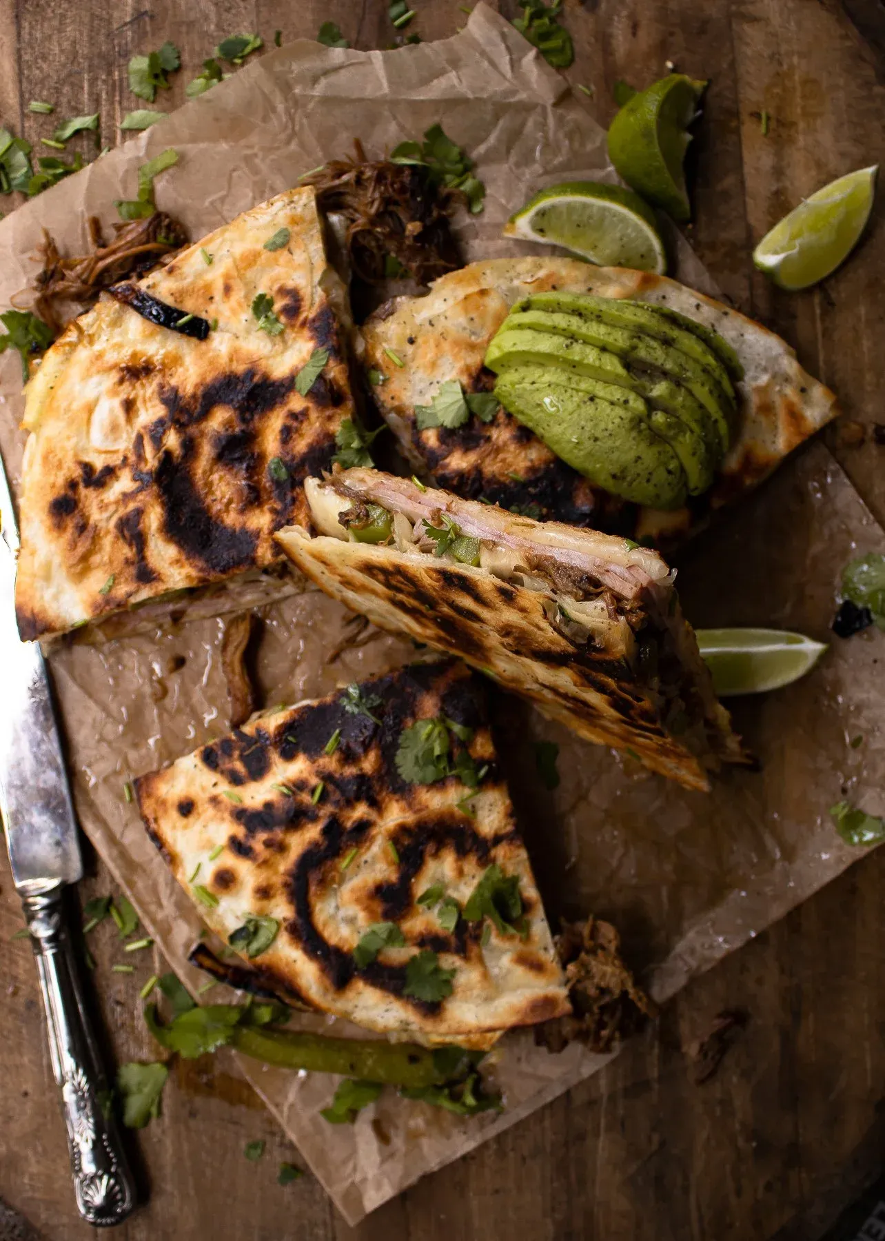 Overhead elevated angle of Cubano Inspired Quesadilla cut into wedges on parchment and dark wood