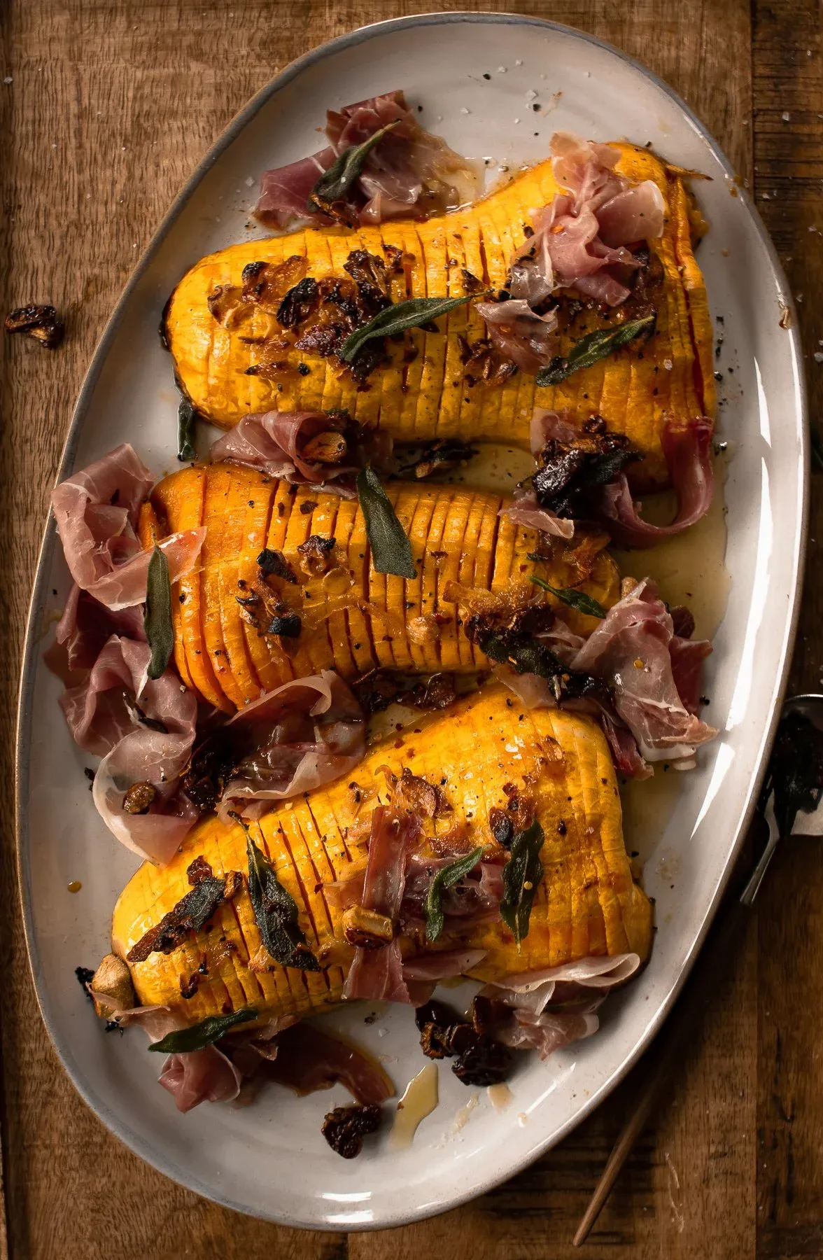 Slightly elevated overhead shot of three hasselback butternut squash halves on a white oval platter