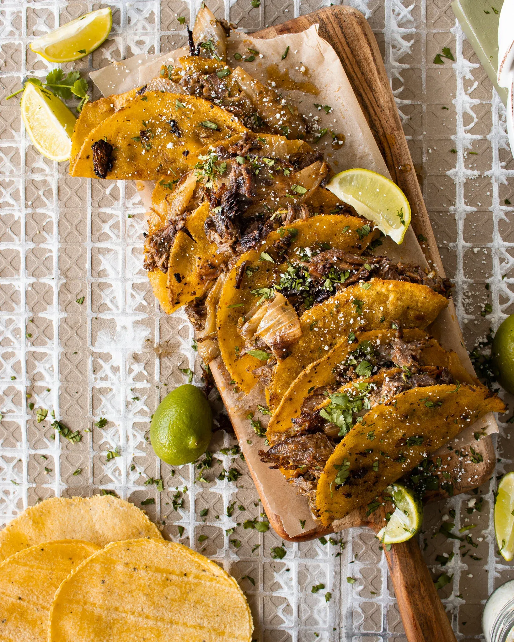 Overhead shot of open-faced Crispy Dominican Beef Tacos fanned across a narrow wooden paddle board