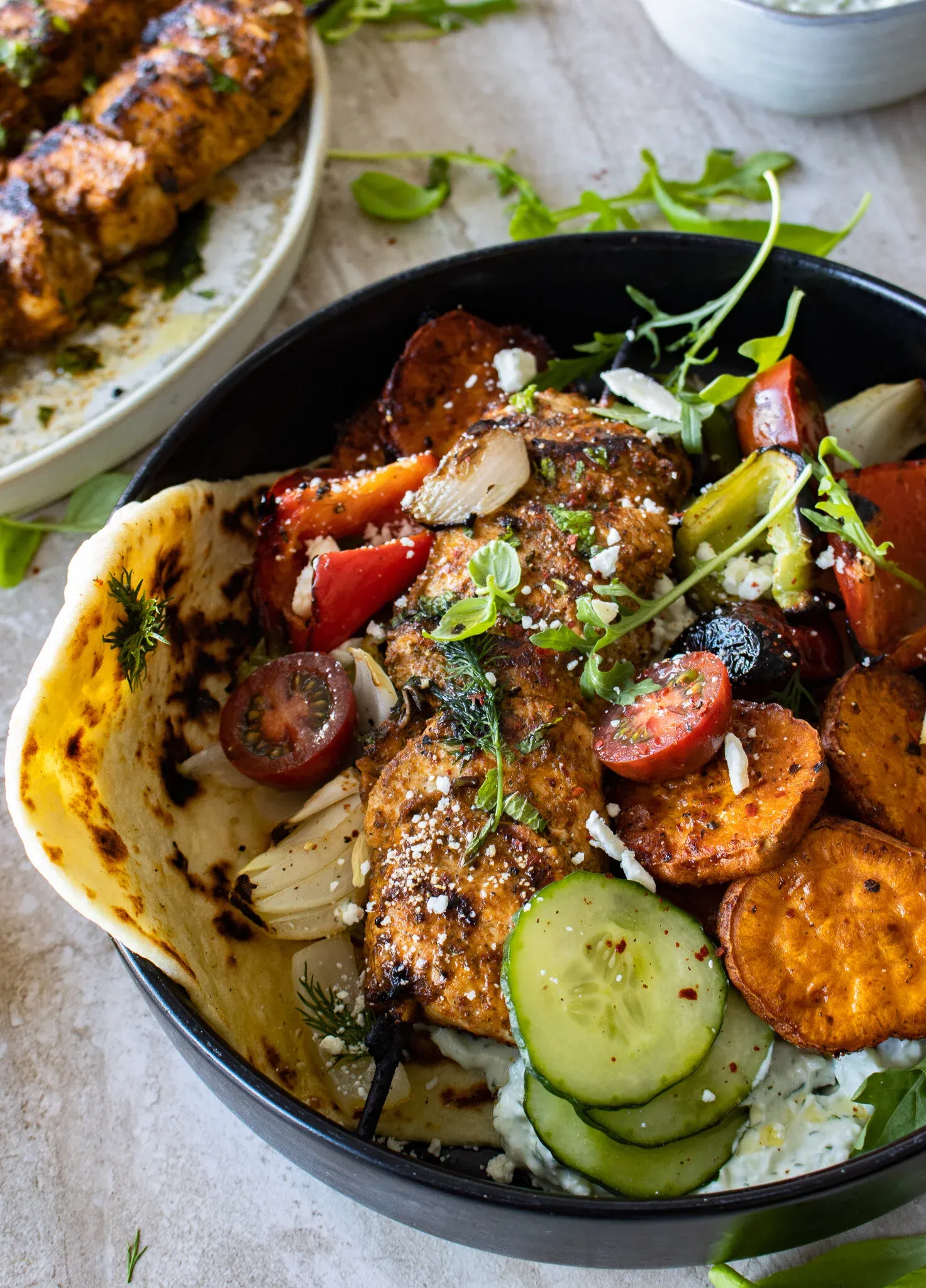 Angled close-up of a black bowl containing chicken and vegetable skewers with roasted sweet potatoes