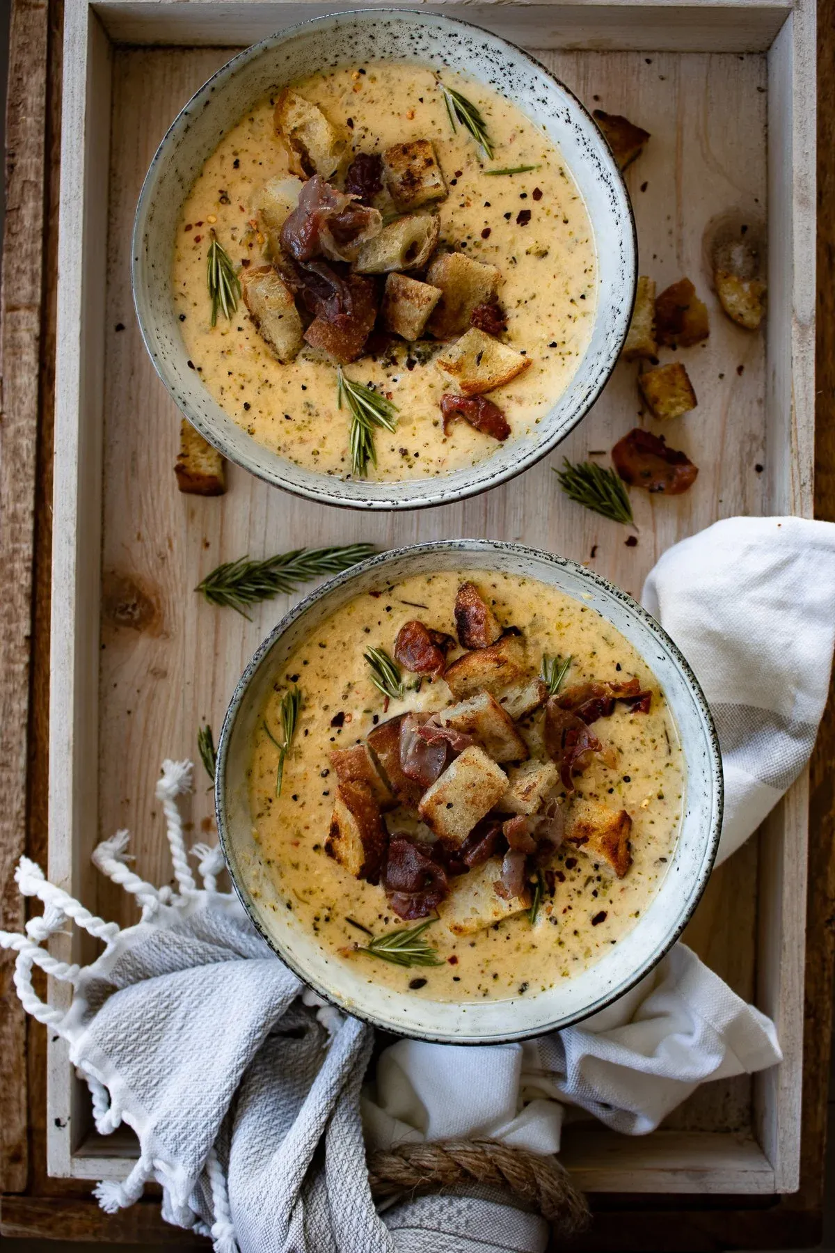 Overhead view of two bowls of finished One Pot Broccoli and Zucchini Cheddar Soup presented in gray speckled bowls inside a light wooden serving tray