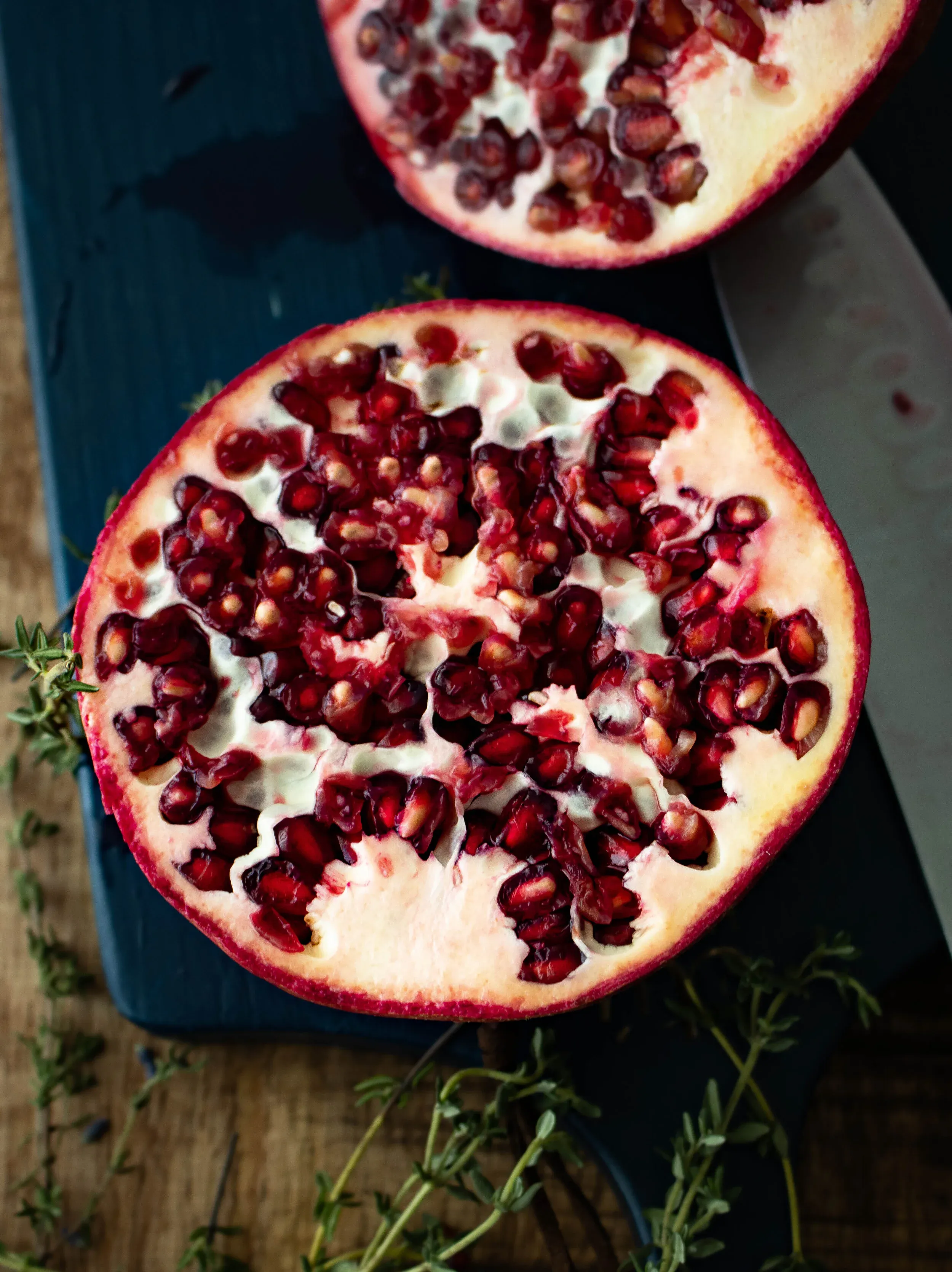Halved pomegranate cut face-up on a dark slate board revealing densely packed deep ruby-red arils against white pith membranes