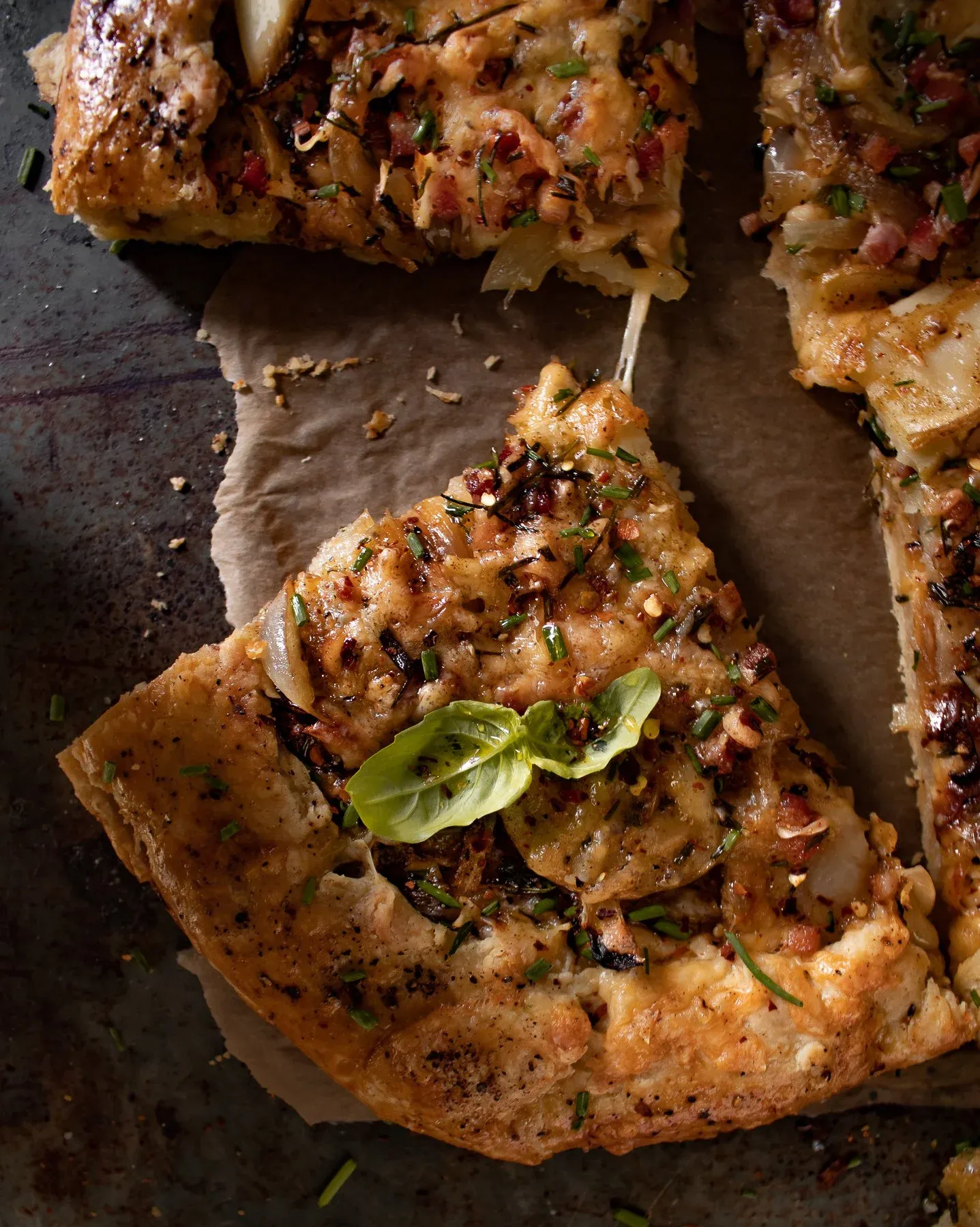 Angled overhead close-up of a wedge slice of cheesy potato tart with pancetta on parchment paper