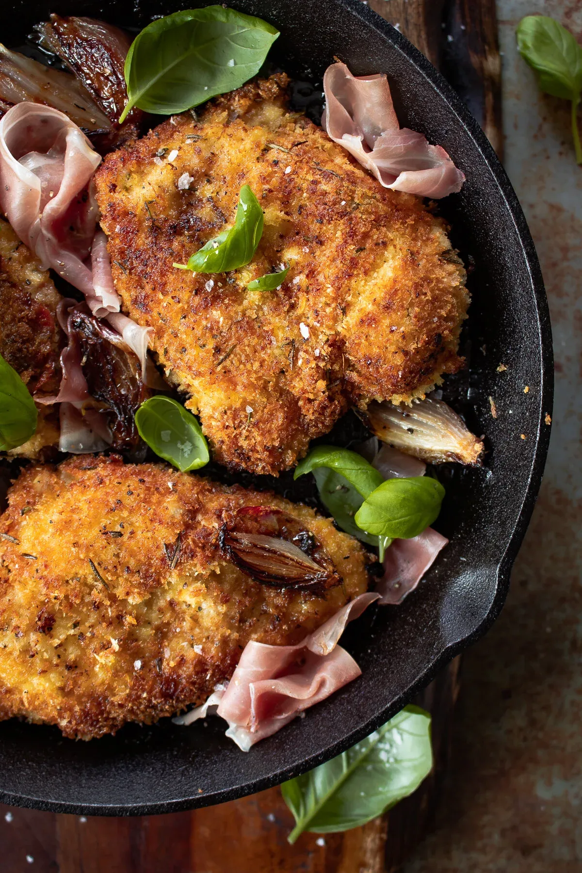 Angled shot of two golden-brown Prosciutto and Basil Wrapped Chicken cutlets in the black cast iron skillet