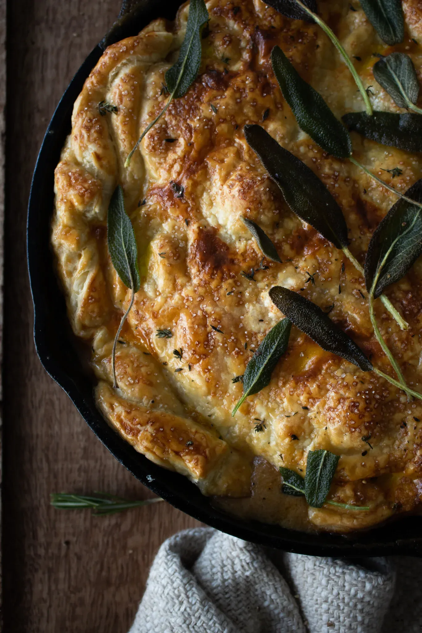 Elevated angled view of the upper half of the cast iron chicken pot pie focusing on the undisturbed golden-amber pastry crust with its buttery caramelized surface