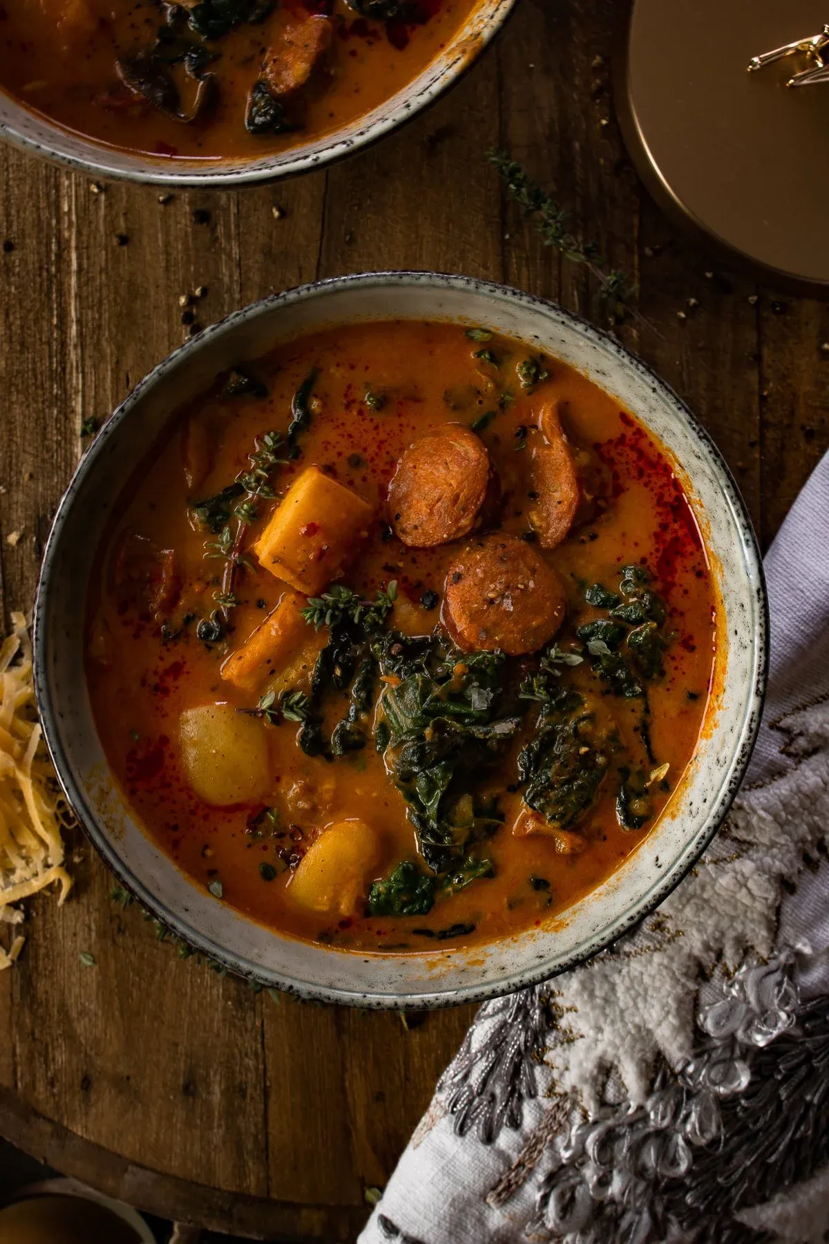 Overhead view of two speckled grey ceramic bowls of Smoked Potato and Sausage Soup on a dark wood lazy-Susan surface