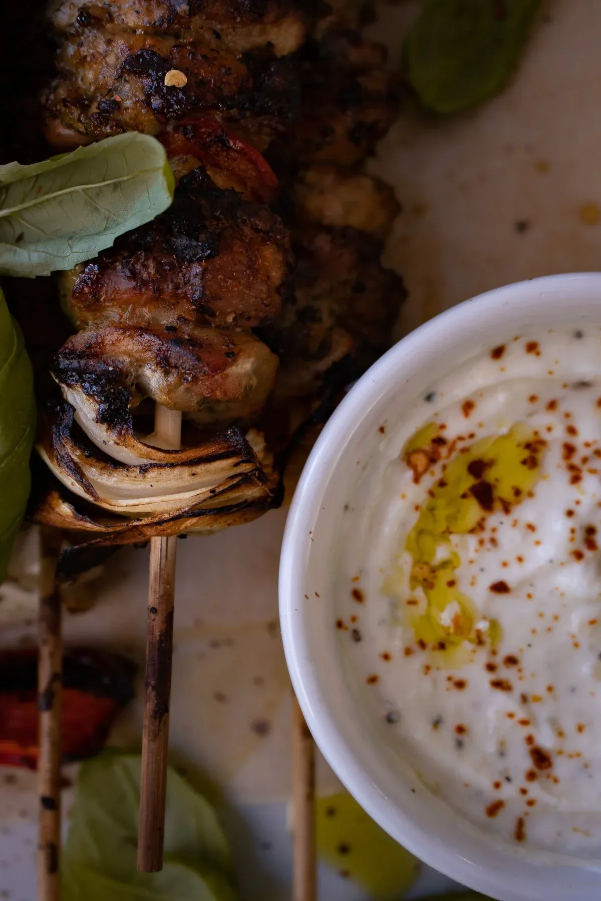 Extreme close-up angled shot of a charred Grilled Chicken Skewer showing deeply caramelized chicken pieces with a grilled onion ring and red pepper at the base of the bamboo stick