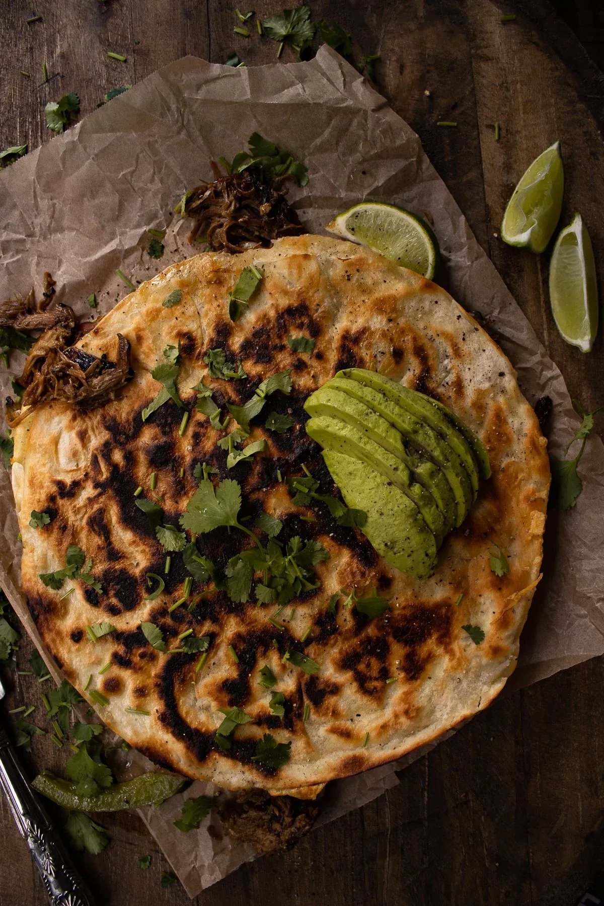Overhead flat-lay of an intact whole Cubano Inspired Quesadilla on crumpled parchment paper atop a dark rustic wood surface