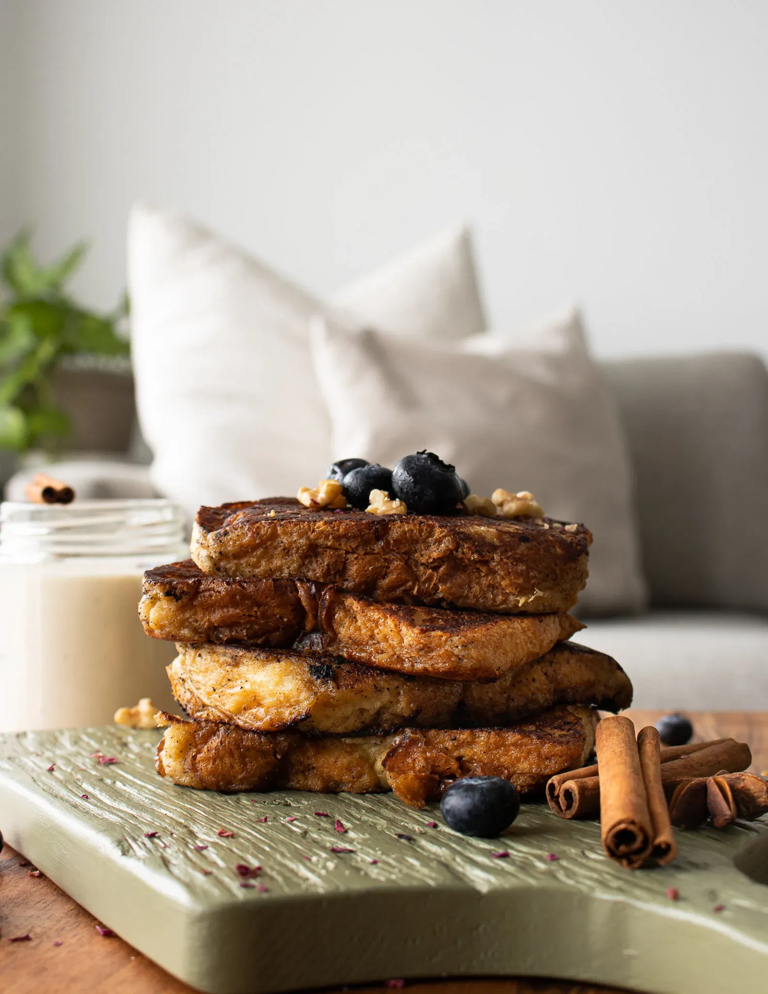 Front-angle portrait of the complete Coquito French Toast stack resting on the sage-green wood board