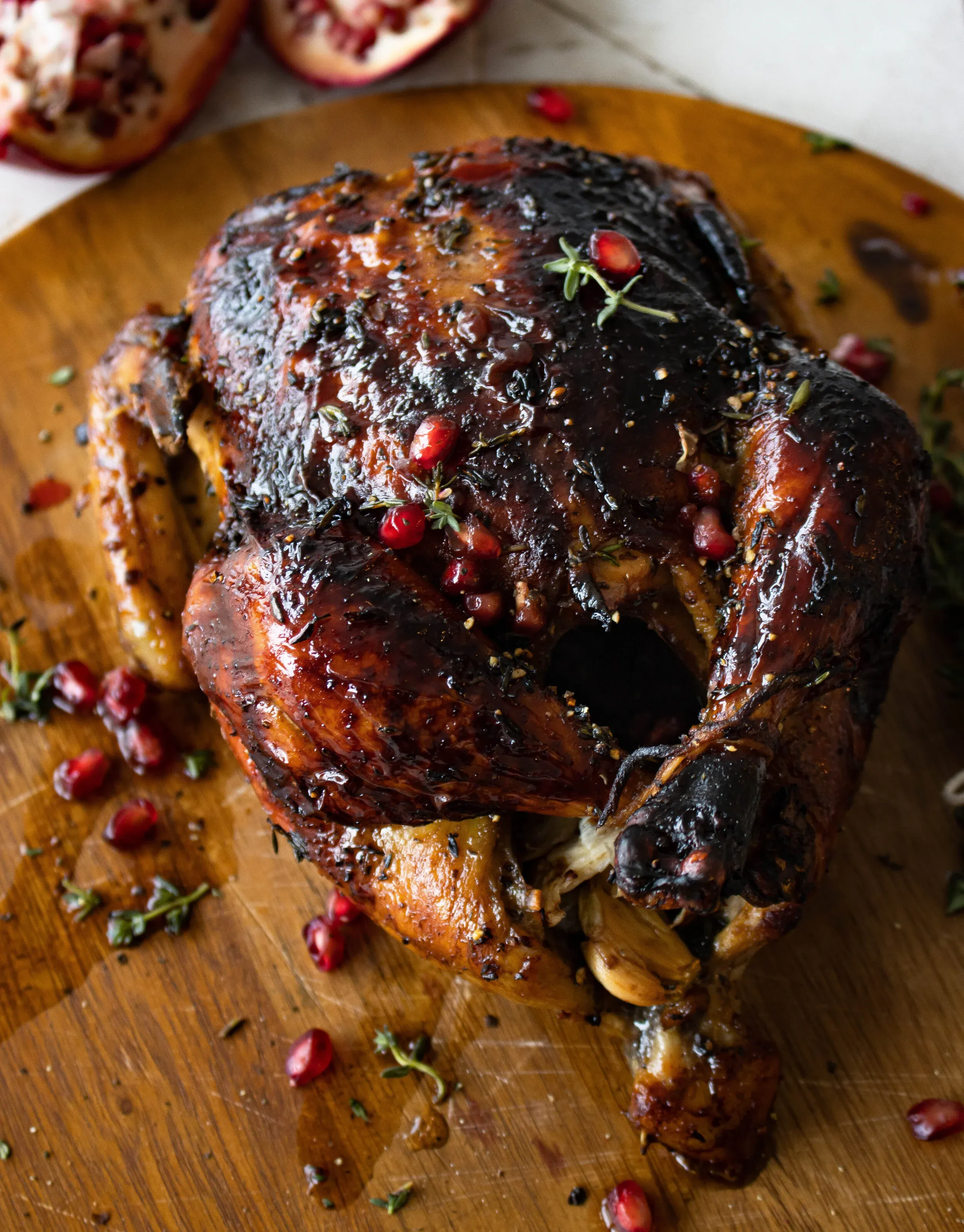 Angled overhead close-up of the whole Balsamic and Pomegranate Roasted Chicken on a round wooden board