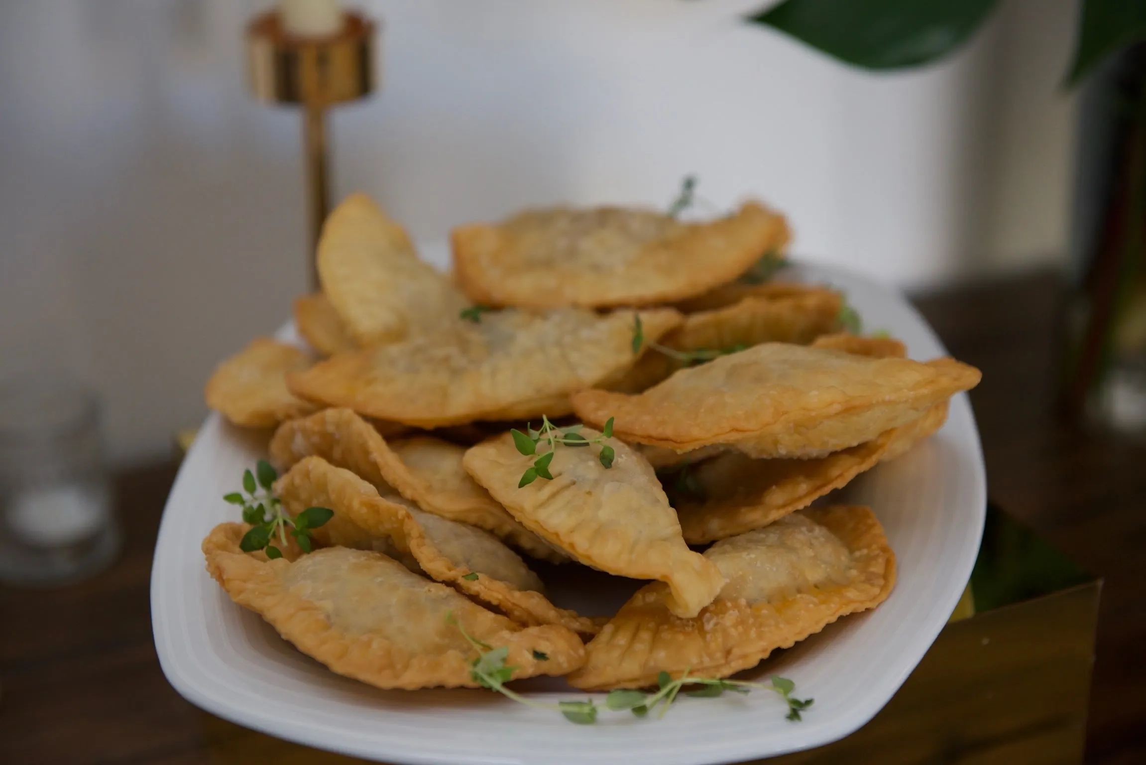 A platter of golden, freshly fried empanadas, scattered with sprigs of thyme.