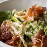 Close-up side-angle of a white bowl of Cacio e Pepe with Spring Veggies and Crispy Prosciutto
