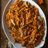 Pasta Alla Vodka piled on a white embossed oval ceramic serving platter on dark wood