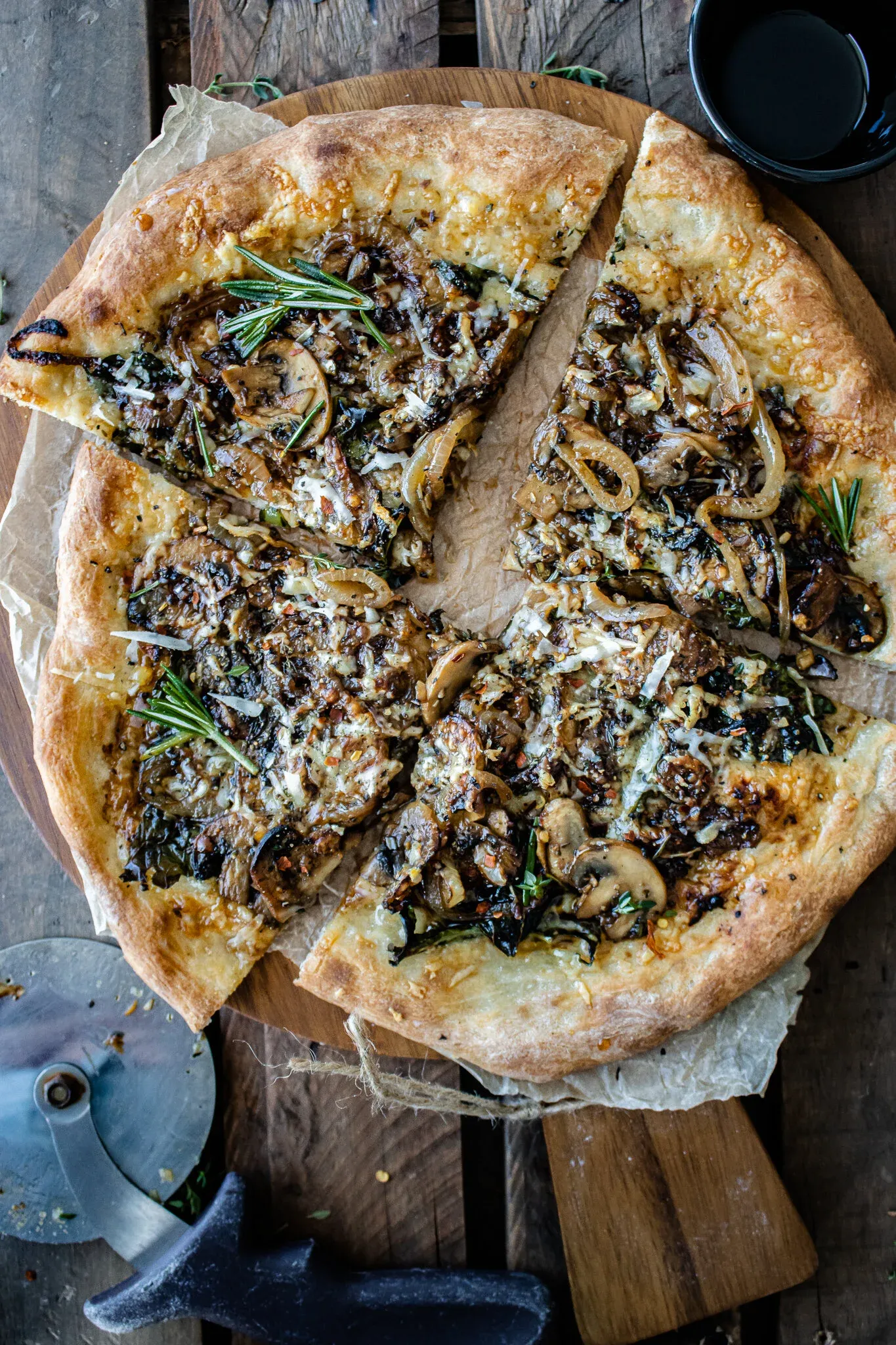 Overhead view of a sliced caramelized onion and mushroom pizza on a round wooden board over parchment paper