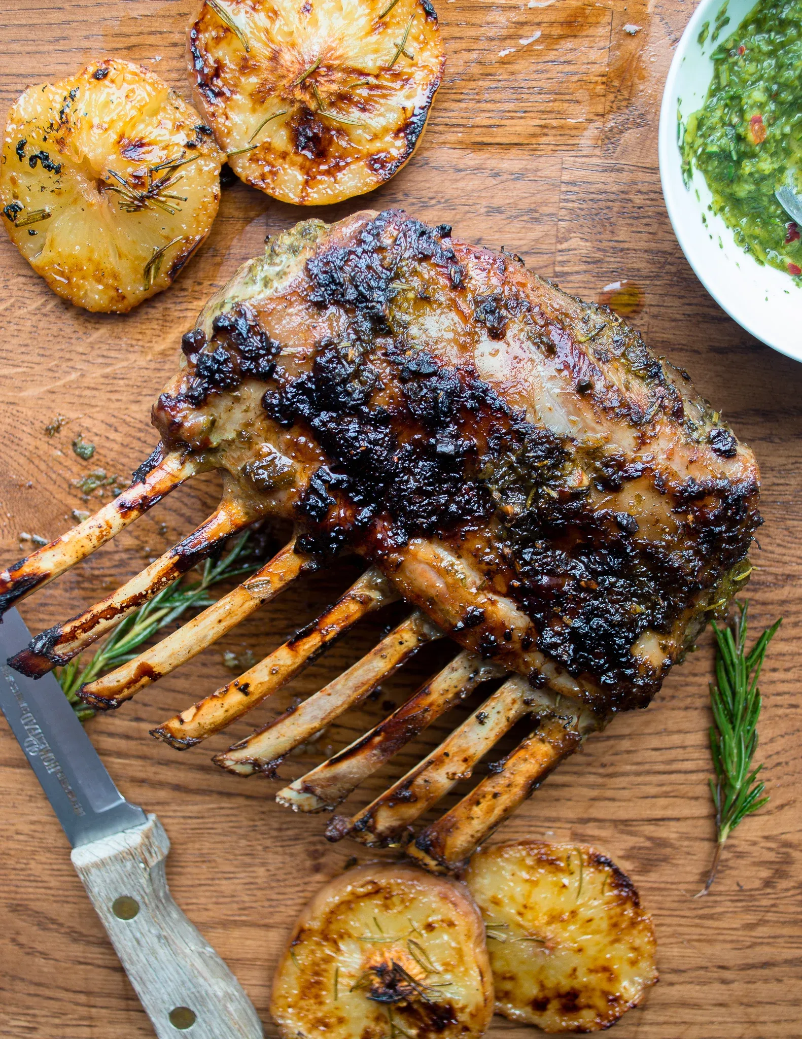 Herb crusted rack of lamb with frenched white rib bones standing upright on a warm wood cutting board