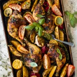 Overhead view of a dark sheet pan of Sheet Pan Dominican Roasted Chicken with Wasakaka on a light stone surface
