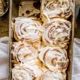 Overhead flat-lay of eight Brown Butter Cinnamon Rolls with Cream Cheese Frosting packed tightly in a worn silver metal baking pan