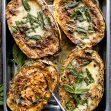 Four halves of Stuffed Spaghetti Squash in a silver metal baking pan, overhead view on a rustic wooden surface