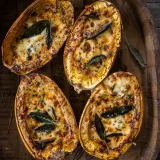 Four halved Mushroom and Sage Cream Stuffed Spaghetti Squash boats arranged on a round wooden barrel tray