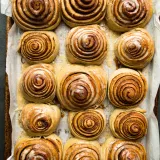 Overhead view of fifteen freshly baked Cinnamon Rolls with Honey Mascarpone Icing arranged in a 3-by-5 grid in a parchment-lined metal baking pan