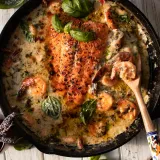 Overhead view of a black cast iron skillet on a white painted wood surface holding Saucy Salmon and Shrimp in Coconut Milk with Spinach