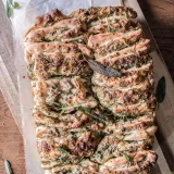 Overhead view of a whole cheesy spinach and artichoke pull-apart bread loaf on parchment paper on a wooden cutting board
