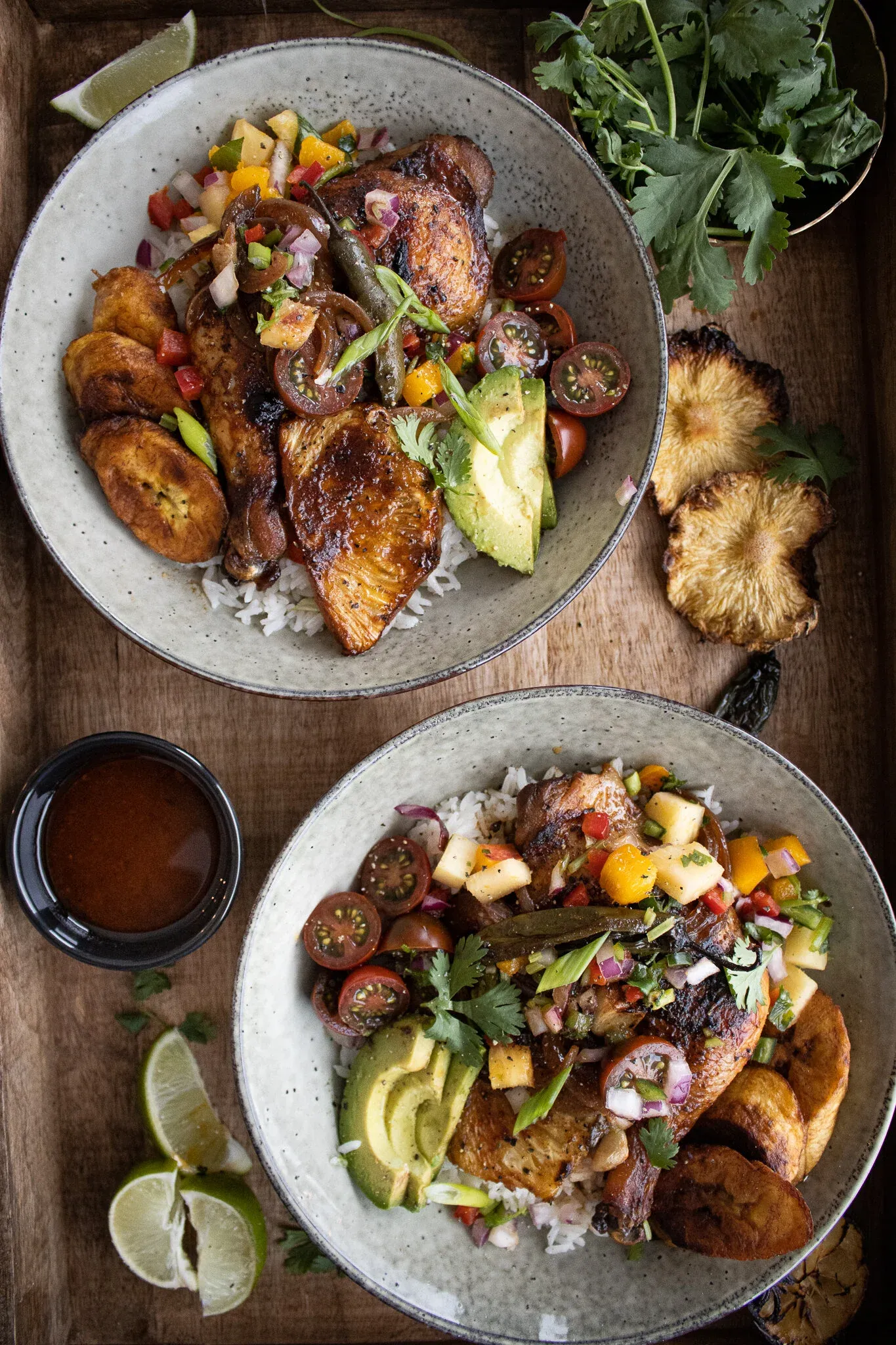 Overhead view of two gray speckled bowls of Sheet Pan Pineapple Chicken Bowls on a wooden tray
