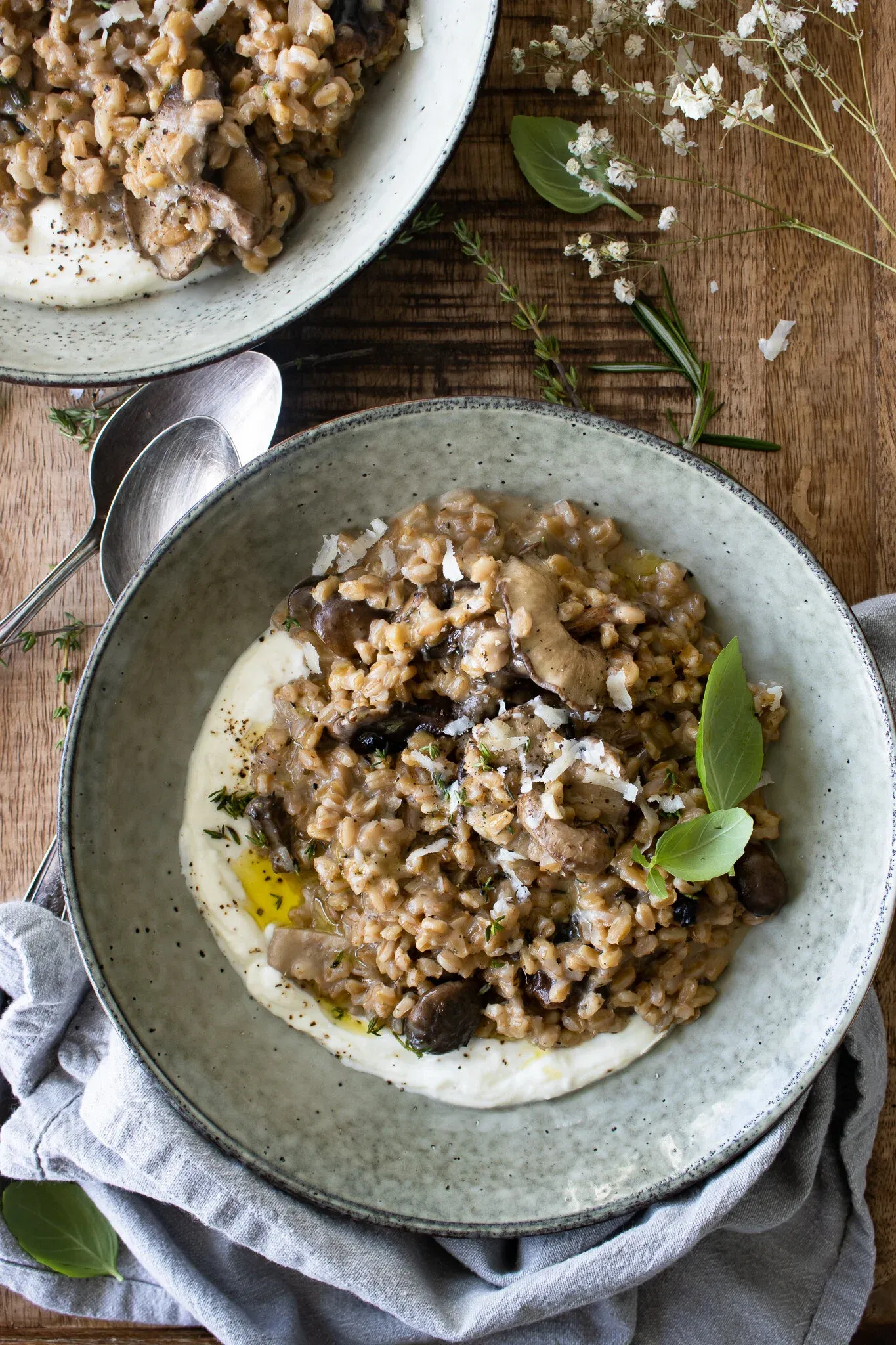 Overhead shot of a grey speckled stoneware bowl of Farro Risotto with Mushrooms and Whipped Ricotta in the foreground