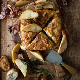 Overhead shot of Wrapped Brie and Prosciutto with Herbed Honey Peaches on a rustic wood cutting board