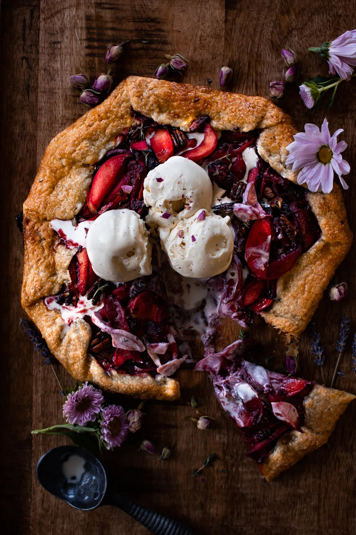 Overhead dark-moody shot of a rustic poached peach galette on a dark wood board