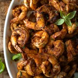 Overhead close-up of a large white oval platter piled high with Cajun-seared shrimp for Cajun Shrimp with Kale Polenta