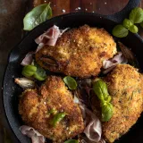 Three golden panko-crusted Prosciutto and Basil Wrapped Chicken breasts in a black cast iron skillet on a wood cutting board