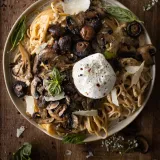Overhead shot of a wide speckled ceramic bowl of mascarpone pasta with roasted mushrooms and burrata