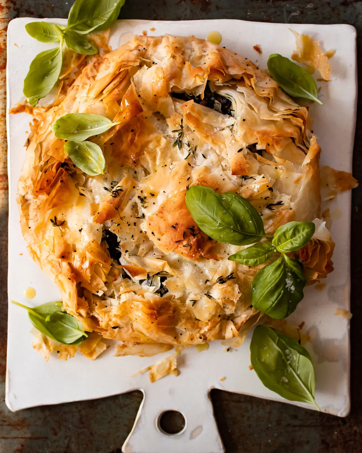 Spinach and Feta Phyllo Pie as a rustic round galette on a white ceramic paddle board, overhead view on a dark background