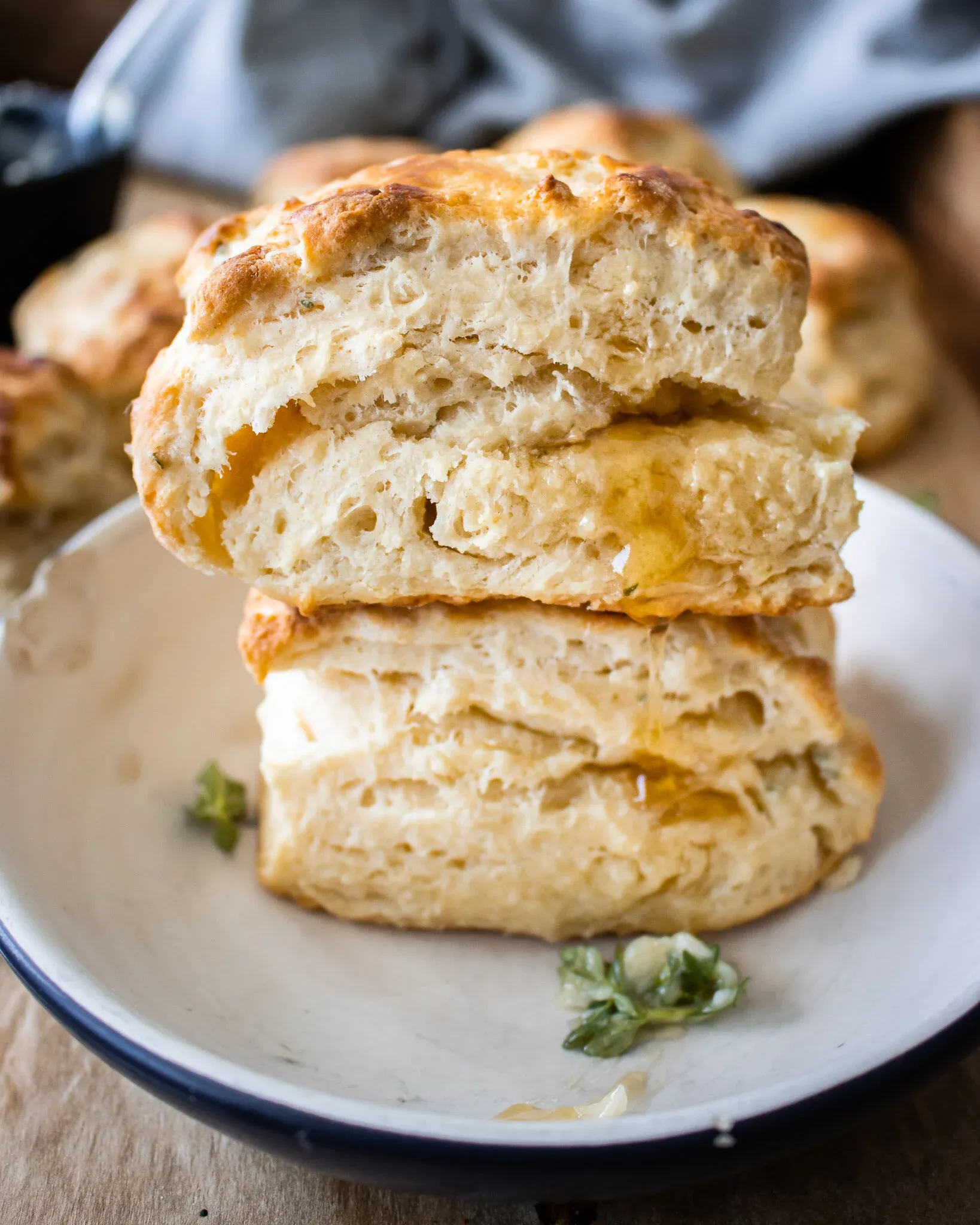 Two lemon thyme buttermilk biscuits stacked on a white enamel plate with a navy blue rim
