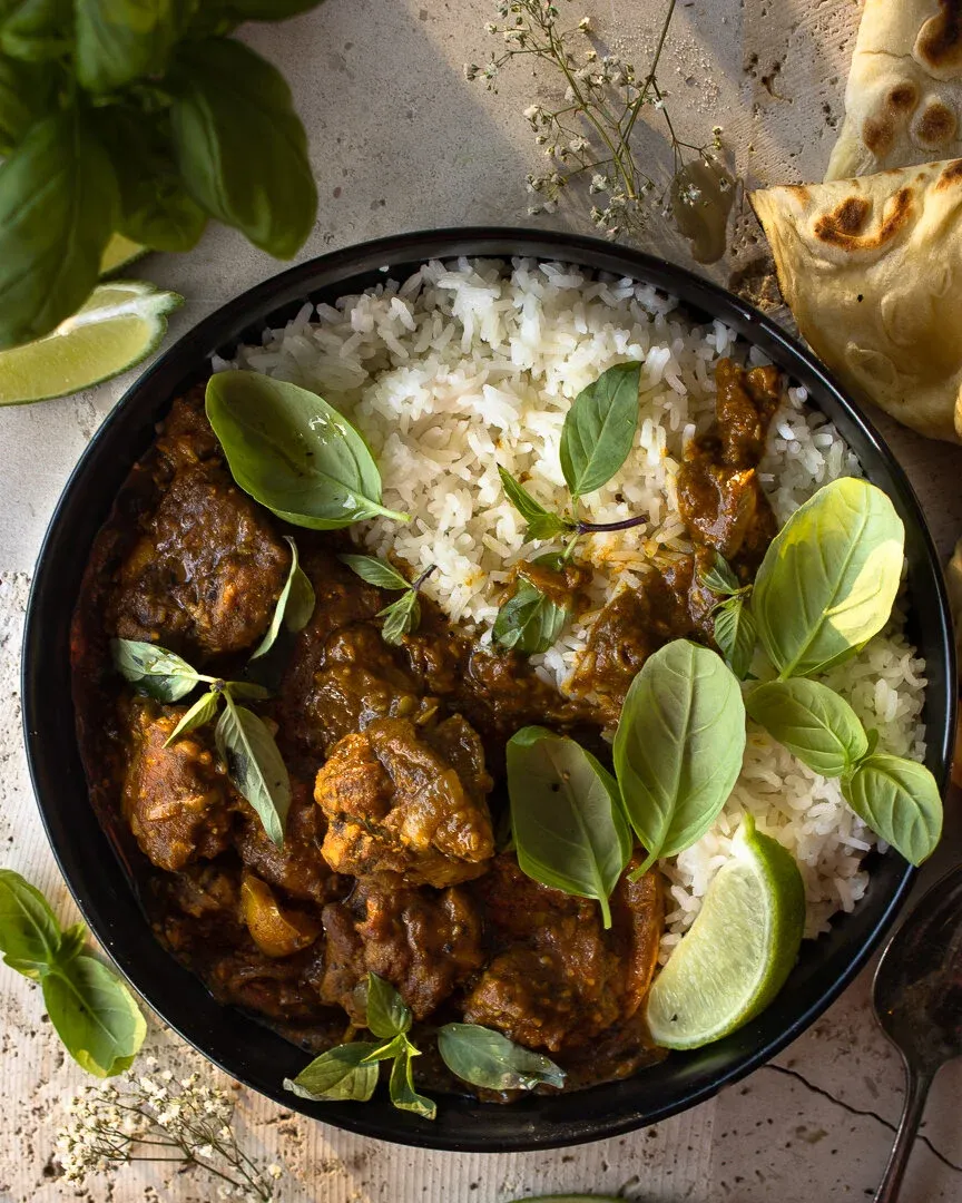 Overhead shot of a matte black bowl of Quick Coconut Curry Chicken on a gray concrete surface